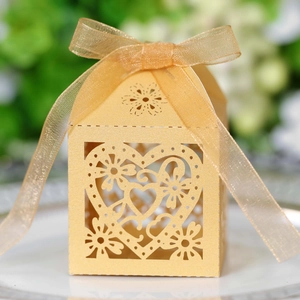 Detail of champagne gold laser-cut heart candy box with silk ribbon on white plate