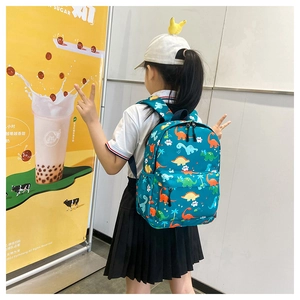Detail showing the dinosaur pattern and side mesh pocket of this kids backpack on a model