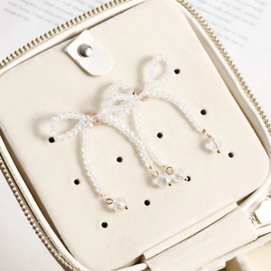 Detail of beaded bow earrings with pearlescent tassels in a cream jewelry box