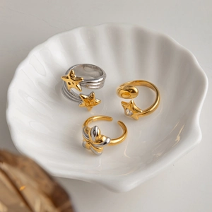 Three-piece set of gold and silver open rings with star and floral charms in a shell tray