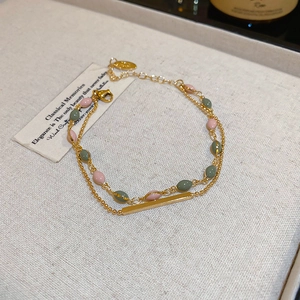 Detail of a double-layered gold bracelet with pink and green enamel beads on fabric