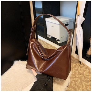 Detail of a brown leather hobo bag featuring golden zippers and wide adjustable straps