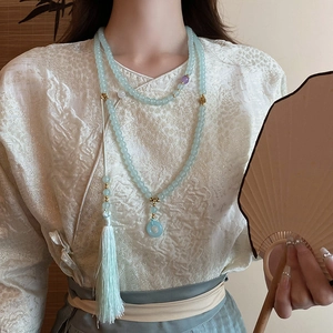 Detail of a light blue glass bead necklace with silk tassels on a white Hanfu outfit