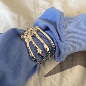 Detail of silver skeleton hand bracelet worn over a blue shirt sleeve in gothic style