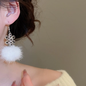Detailed view of acrylic snowflake earrings with soft white pom-poms worn by a model