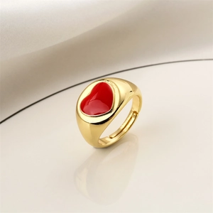 Detailed view of an adjustable gold-plated ring with a red enamel heart on a sleek surface