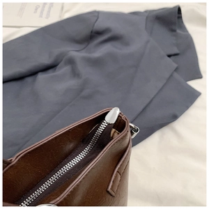 Detail of a brown leather tote bag with a silver metal zipper and stitching detail