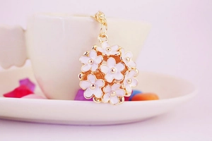 Close-up of white daisy flower cluster keychain with gold-tone metal edges on a ceramic cup