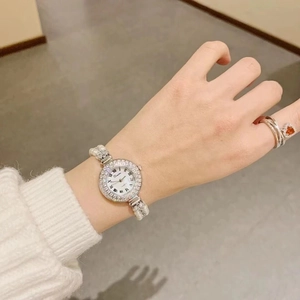 Elegant woman wearing a pearl strap watch with crystal bezel and a red heart gemstone ring