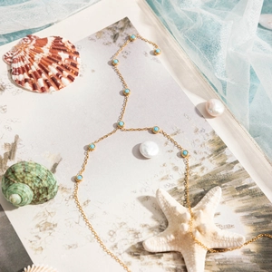 Vue détaillée d'un collier en chaîne dorée avec pierres turquoise sur un fond marin