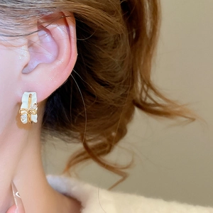Detail of 18k gold plated C-shaped earring with bowknot and diamond on female ear