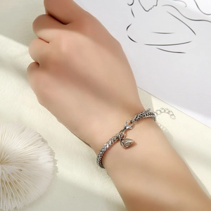 Detail of silver chain bracelet with red woven cord and small heart charm on wrist