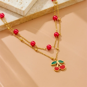 Elegant gold-plated double-layer cherry necklace with red beads on a textured stone surface