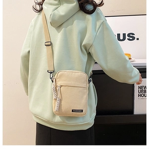 Detail of beige canvas crossbody bag featuring adjustable strap and fashion label