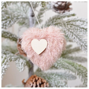 Close-up of pink fluffy plush heart ornament with gold tinsel on a snowy Christmas tree