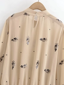 Détails de paillettes et broderies florales sur haut en mousseline beige à col montant