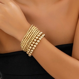 Detail shot of multi-layer gold beaded bracelet set on wrist with metallic heart pendant