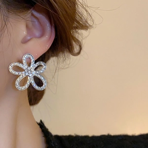 Macro shot of silver floral earrings with hollow petals and sparkling diamonds on model