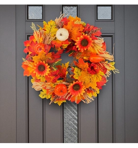 Close-up of autumn harvest wreath with maple leaves sunflowers and pumpkins on a dark door