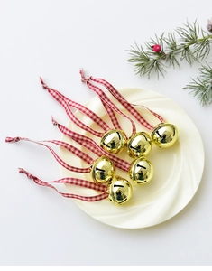 Close-up of six gold Christmas bells with red and white ribbons on a white ceramic plate