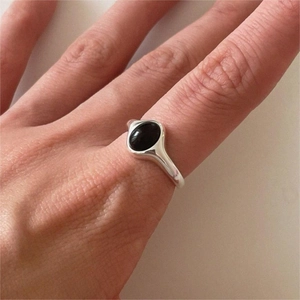 Close-up of minimalist silver ring with oval black agate stone worn on finger