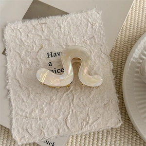 Detail of wavy cream hair claw clip with pearlescent finish and gold metal teeth