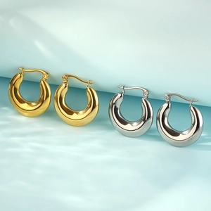 Macro detail of glossy gold and silver oval hoop earrings on light blue background