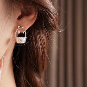 Close-up of a silver basket-shaped stud earring with bow detail on a female model