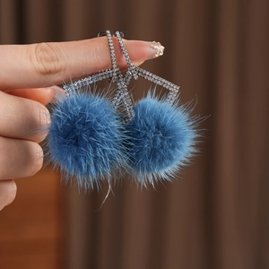 Detail of blue pompom earrings with geometric rhinestone frame and plush texture