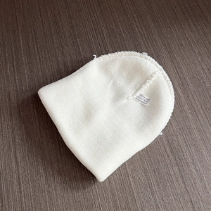 Pure white knitted beanie for kids with heart patch on a gray wood background