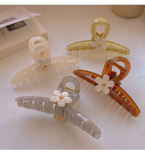 Detailed view of four large acrylic floral hair claws in ivory, amber, and grey colors