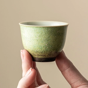 Hand holding green glaze ceramic teacup with retro mottled finish and rustic brown base