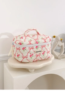 Close-up of quilted floral makeup bag featuring pink roses, ribbons and a top handle