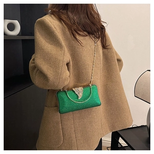 Green glitter evening bag with gold chain strap worn by a model in a stylish coat