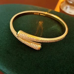 Macro detail of gold-plated open bangle with pavé zircons and green gemstone accents