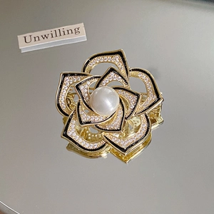 Close-up of 14k gold plated camellia brooch with black enamel petals and pearl center