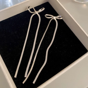 Macro shot of silver bow knot earrings with long snake chain tassels on velvet padding