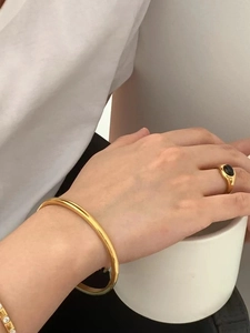 Polished gold cuff bracelet with a black gemstone signet ring held by a hand on a cup