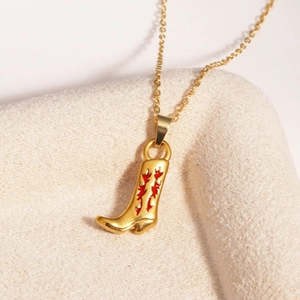 Gros plan d'un pendentif botte de cow-boy doré avec émail rouge sur velours beige