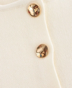 Détail du tissu en maille blanc crème avec d'élégants boutons sphériques en métal doré