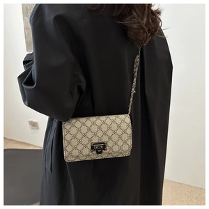 Detail view of beige crossbody bag with monogram pattern, metal lock, and chain strap