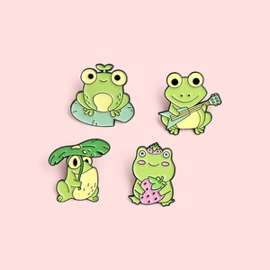 Detail view of cute cartoon frog enamel pins set featuring strawberry and guitar designs