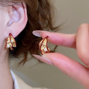 Close-up of golden petal earrings with red enamel and pearl on model's ear