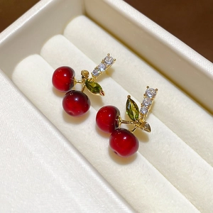 Vue macro de boucles d'oreilles cerises avec perles rouge foncé et pierres feuilles vertes