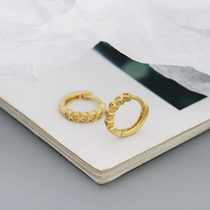 Close-up of gold heart hoop earrings with clear zircons on a white paper background