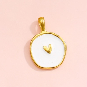 Close-up of circular gold-plated alloy pendant with white enamel and a small gold heart