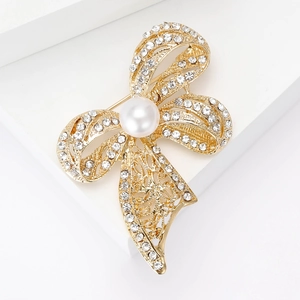 Elegant gold bow brooch with sparkling rhinestones and a central pearl on white background