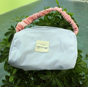 Detail of light blue corduroy makeup bag with a contrasting pink pleated handle