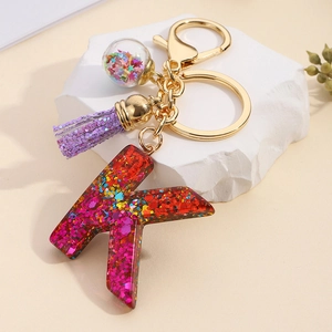 Detail of glitter resin letter K keychain with purple tassel and star bottle charm