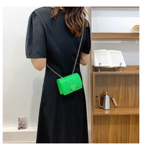 Detail of neon green mini crossbody bag with heart buckle and gold chain on model